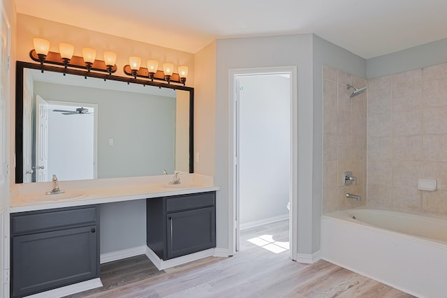 bathroom featuring hardwood / wood-style flooring, ceiling fan, vanity, and tiled shower / bath