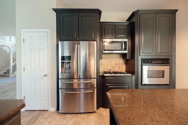 kitchen featuring tasteful backsplash, appliances with stainless steel finishes, dark stone countertops, and light tile patterned flooring