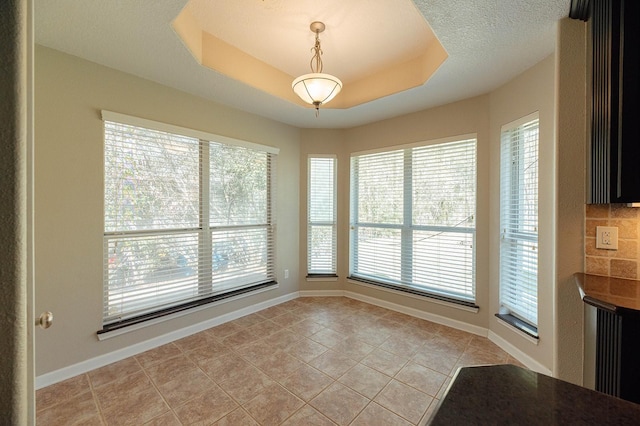 unfurnished dining area with a raised ceiling, a healthy amount of sunlight, baseboards, and light tile patterned flooring