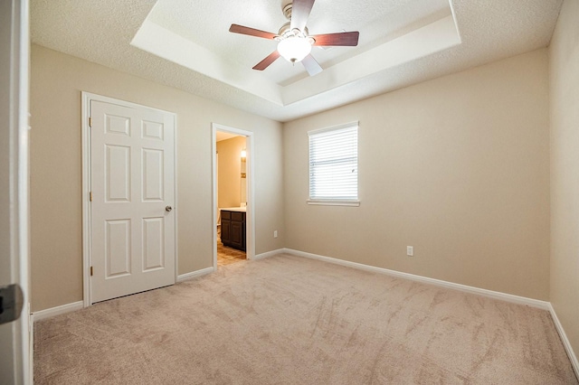 unfurnished bedroom featuring light carpet, baseboards, ensuite bath, a tray ceiling, and a textured ceiling