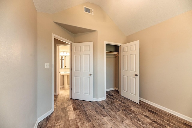 unfurnished bedroom featuring lofted ceiling, dark wood-style flooring, visible vents, and baseboards