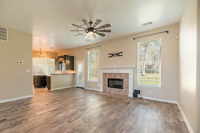 unfurnished living room featuring dark wood-style floors, a fireplace, visible vents, a ceiling fan, and baseboards