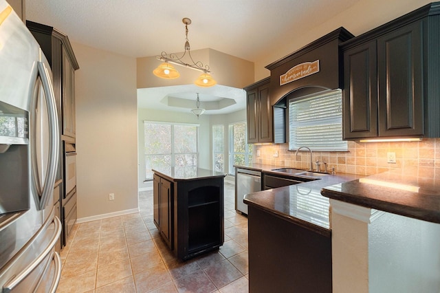 kitchen featuring stainless steel appliances, a sink, a tray ceiling, dark countertops, and decorative light fixtures