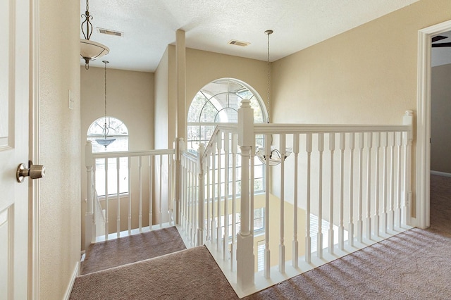 hall with carpet floors, visible vents, a textured ceiling, and a textured wall