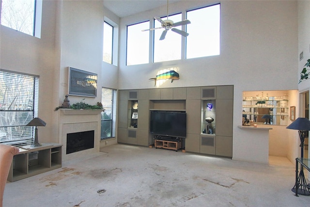 living room featuring ceiling fan, a fireplace, and a high ceiling