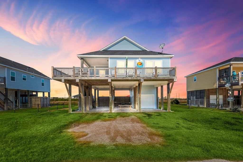 back house at dusk with a yard, a garage, a carport, and a deck