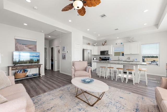 living room with dark hardwood / wood-style floors, ceiling fan, and a tray ceiling