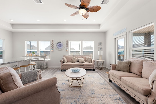 living room featuring a tray ceiling, wood-type flooring, and plenty of natural light