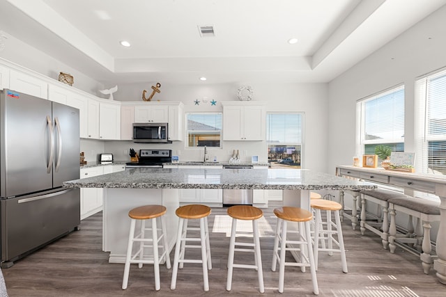 kitchen with white cabinetry, appliances with stainless steel finishes, a center island, and a kitchen bar