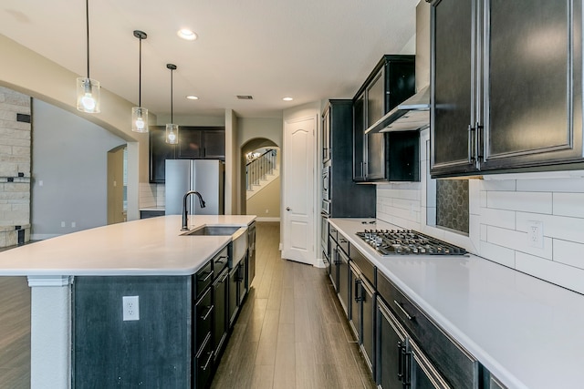 kitchen featuring pendant lighting, appliances with stainless steel finishes, decorative backsplash, sink, and a kitchen island with sink