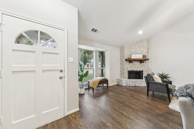 foyer entrance featuring lofted ceiling, a healthy amount of sunlight, dark wood-type flooring, and a stone fireplace