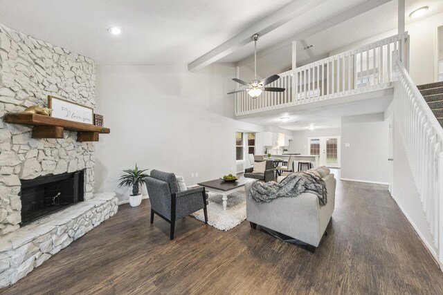 living room featuring ceiling fan, a high ceiling, dark wood-type flooring, a fireplace, and beam ceiling