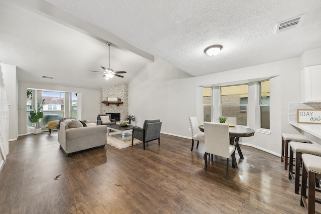 living room featuring ceiling fan, a fireplace, lofted ceiling with beams, dark wood-type flooring, and a textured ceiling