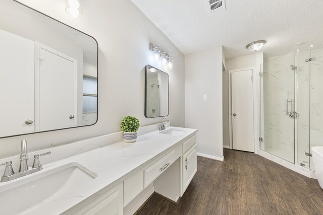 bathroom with a textured ceiling, walk in shower, wood-type flooring, and vanity