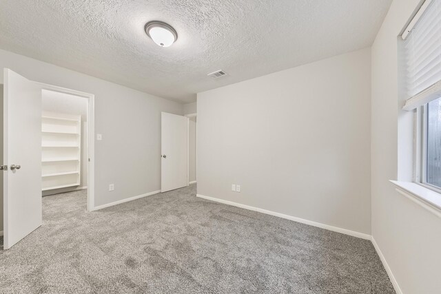 unfurnished bedroom featuring a spacious closet, a closet, a textured ceiling, and light colored carpet