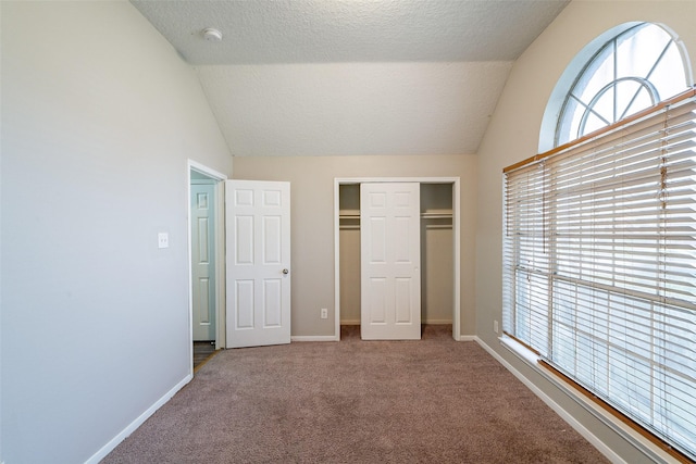 unfurnished bedroom with carpet, a closet, vaulted ceiling, and a textured ceiling