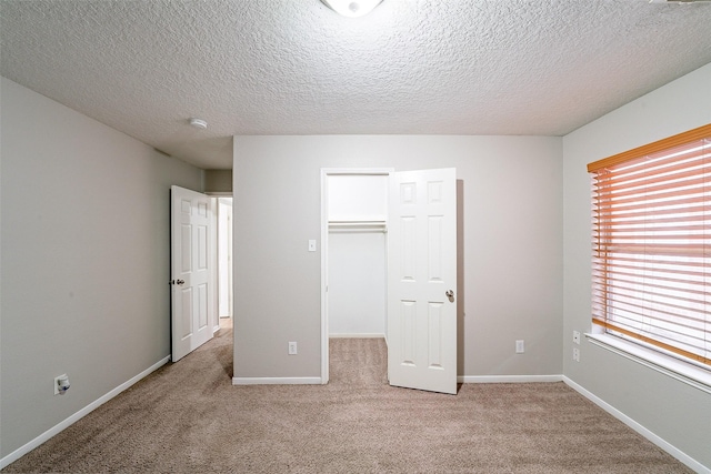 unfurnished bedroom featuring light carpet, a closet, a walk in closet, and a textured ceiling