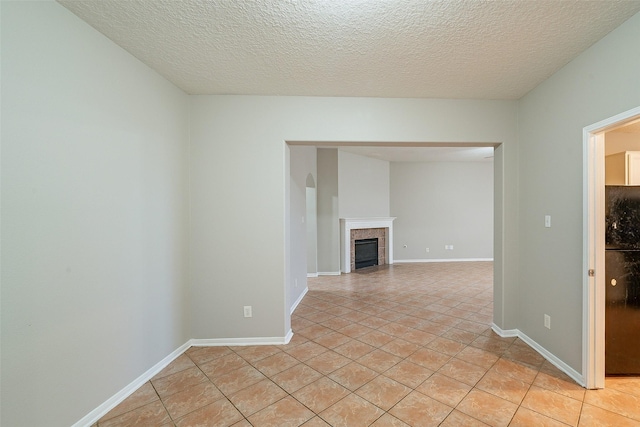 empty room featuring a tile fireplace, a textured ceiling, and light tile patterned flooring