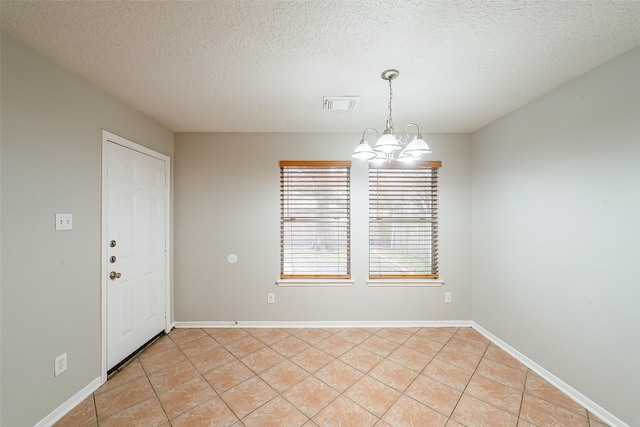 tiled empty room with a textured ceiling and a chandelier