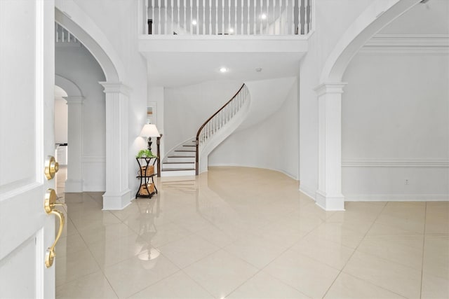 tiled entrance foyer with ornate columns, ornamental molding, and a towering ceiling