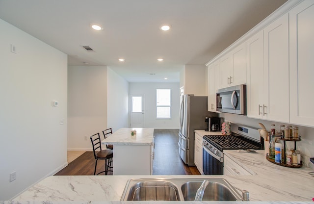 kitchen featuring appliances with stainless steel finishes, a kitchen island, white cabinetry, light stone counters, and a breakfast bar area