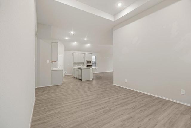 unfurnished living room featuring recessed lighting, a sink, light wood-style flooring, and baseboards