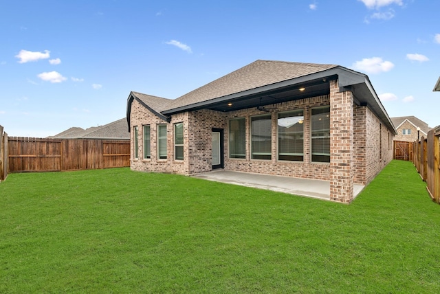 back of property with brick siding, a yard, a shingled roof, a patio area, and a fenced backyard