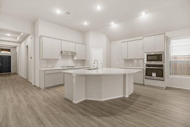 kitchen featuring under cabinet range hood, a sink, light countertops, appliances with stainless steel finishes, and an island with sink