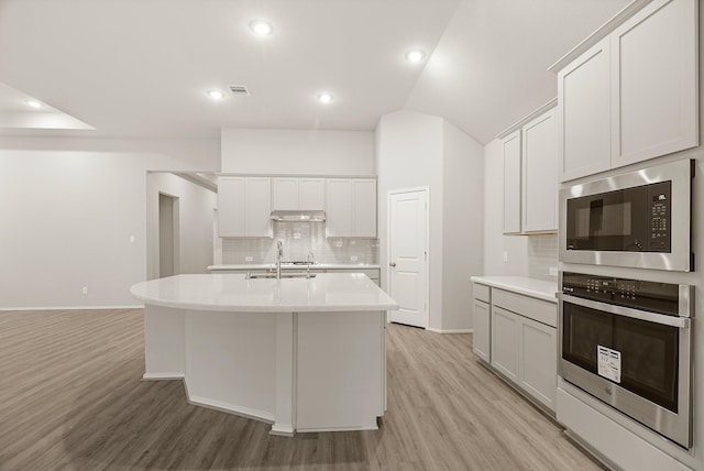 kitchen featuring a kitchen island with sink, light countertops, oven, and built in microwave