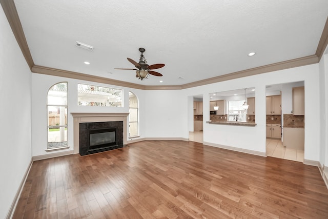 unfurnished living room with a textured ceiling, ceiling fan, crown molding, and light hardwood / wood-style flooring