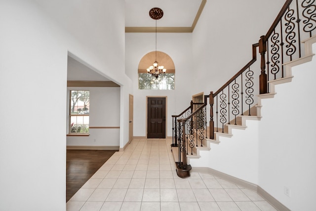 tiled foyer entrance with a notable chandelier, a high ceiling, and ornamental molding