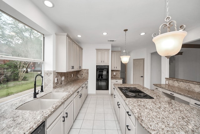 kitchen featuring black appliances, decorative light fixtures, sink, backsplash, and light stone counters