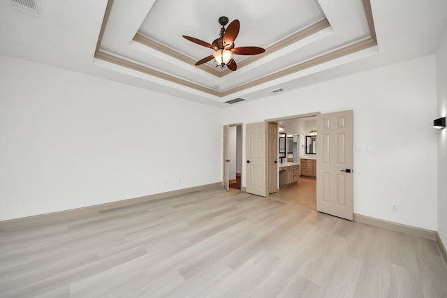 unfurnished bedroom featuring ceiling fan, a raised ceiling, ensuite bath, crown molding, and light hardwood / wood-style flooring