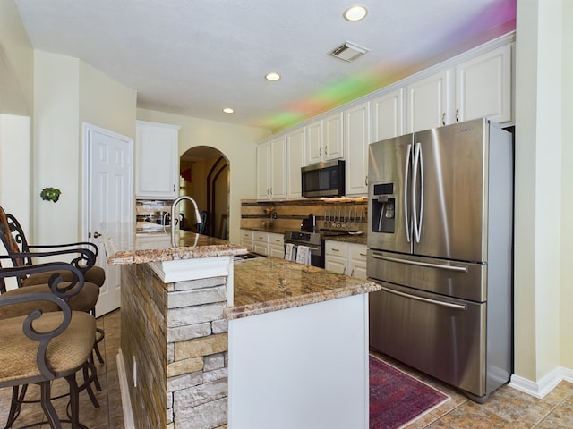 kitchen with a center island with sink, white cabinetry, stone countertops, and appliances with stainless steel finishes