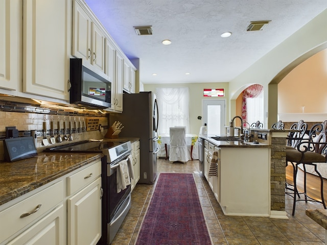 kitchen with appliances with stainless steel finishes, tasteful backsplash, a wealth of natural light, dark stone countertops, and a center island with sink