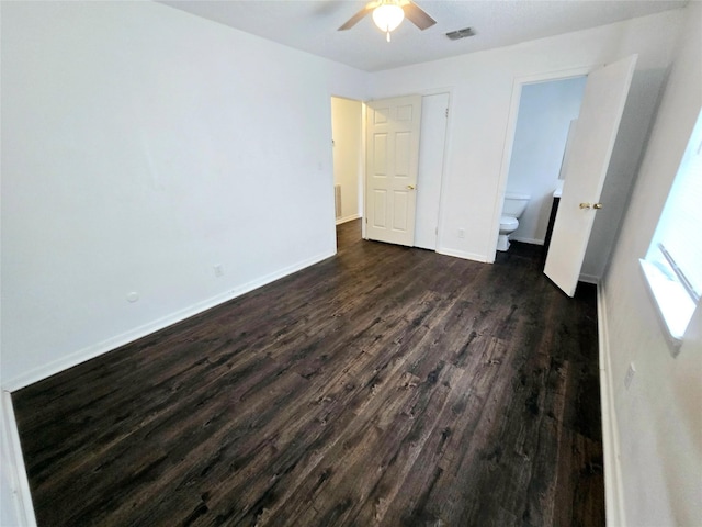 unfurnished bedroom featuring visible vents, dark wood-type flooring, connected bathroom, ceiling fan, and baseboards