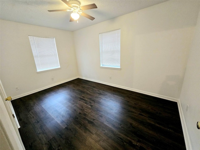 unfurnished room featuring baseboards, a ceiling fan, dark wood-type flooring, a textured ceiling, and a wealth of natural light