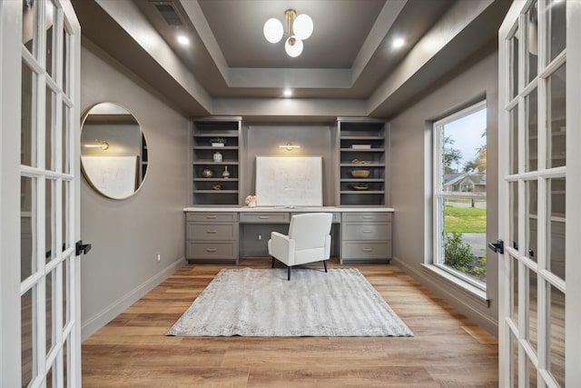 home office featuring built in desk, french doors, a tray ceiling, and light hardwood / wood-style flooring