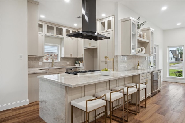 kitchen featuring light stone countertops, hardwood / wood-style floors, white cabinets, and island range hood