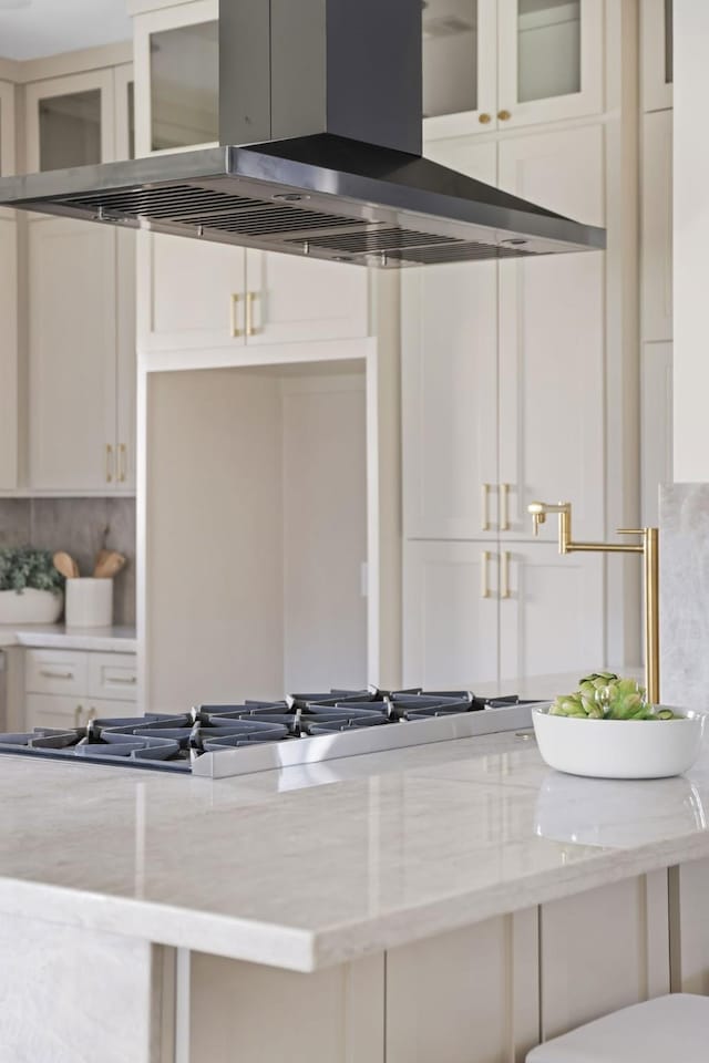 details with tasteful backsplash, white cabinets, light stone countertops, and island exhaust hood