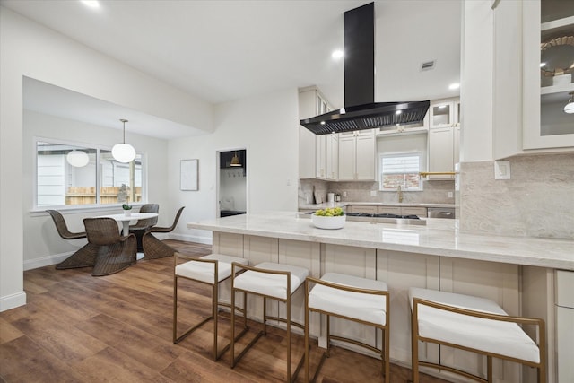 kitchen featuring a breakfast bar area, white cabinetry, wall chimney exhaust hood, and light stone countertops