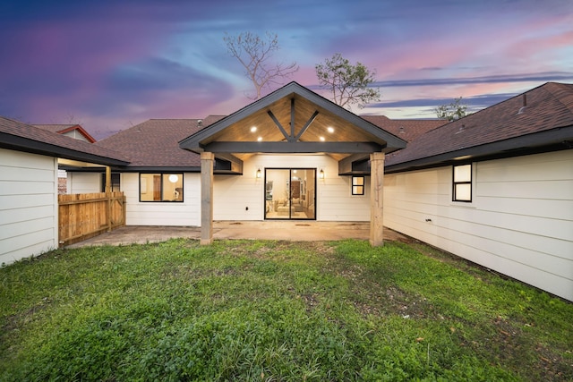 back house at dusk featuring a yard and a patio