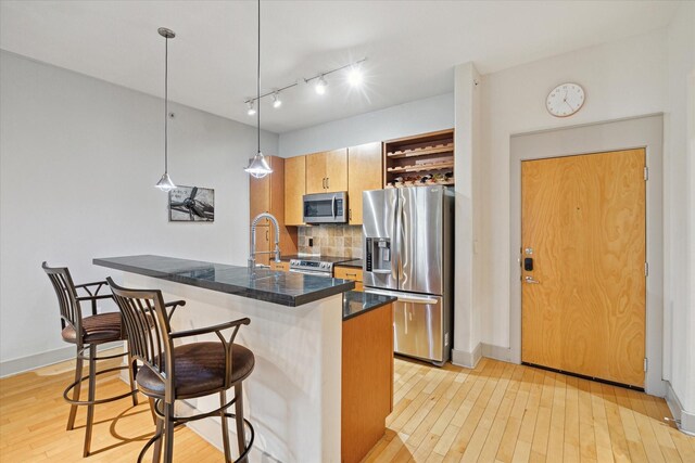 kitchen with light hardwood / wood-style floors, stainless steel appliances, backsplash, decorative light fixtures, and a kitchen breakfast bar