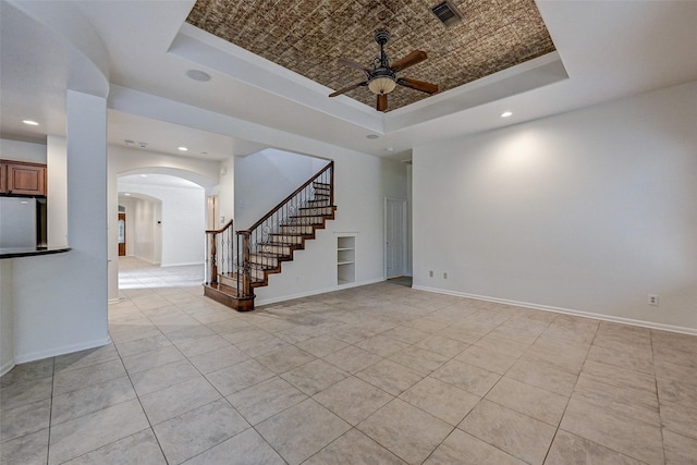 unfurnished living room featuring ceiling fan, light tile patterned floors, a tray ceiling, and built in shelves