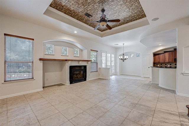 unfurnished living room featuring ceiling fan with notable chandelier, light tile patterned floors, a tray ceiling, and ornamental molding