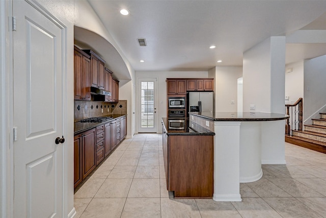 kitchen with appliances with stainless steel finishes, a kitchen island, dark stone counters, tasteful backsplash, and light tile patterned floors