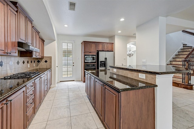 kitchen with dark stone countertops, a center island, decorative backsplash, light tile patterned flooring, and stainless steel appliances