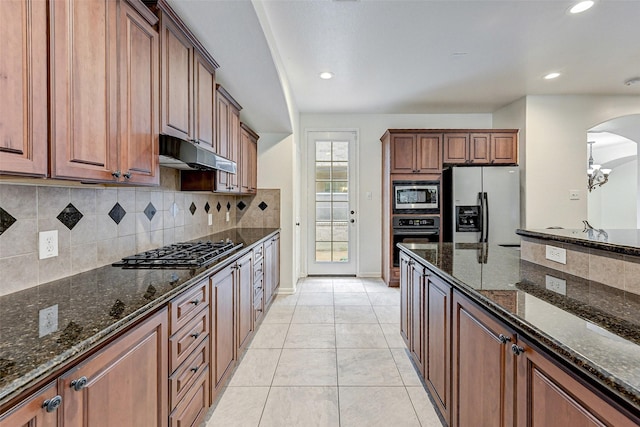 kitchen with tasteful backsplash, dark stone countertops, stainless steel appliances, light tile patterned floors, and a chandelier