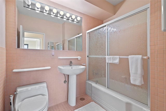 full bathroom featuring toilet, bath / shower combo with glass door, tile walls, tile patterned floors, and sink