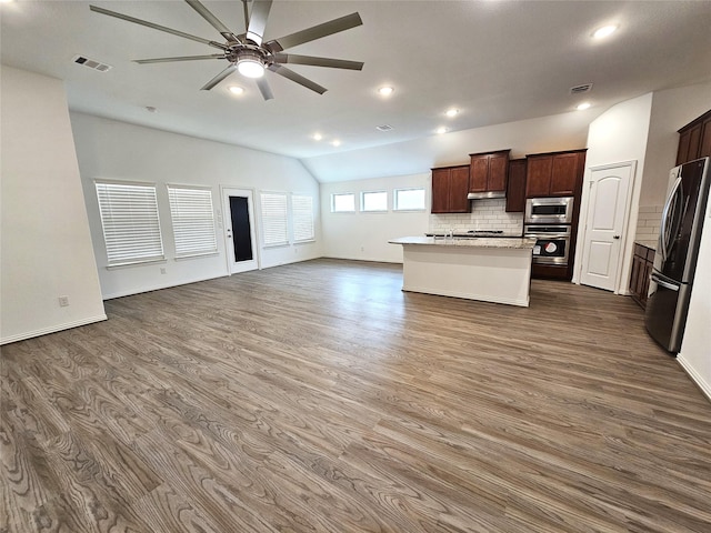 kitchen with lofted ceiling, a center island with sink, decorative backsplash, appliances with stainless steel finishes, and dark wood-type flooring